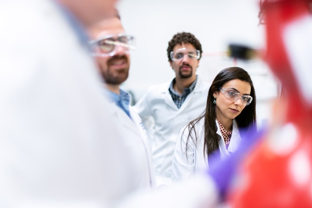 three researchers wearing safety goggles listening to another researcher